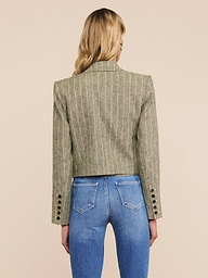 A person with long blonde hair is seen from behind, wearing the Lila Linen-Blend Blazer with pinstripes and buttoned cuffs, paired with blue jeans. The background is plain and light-colored.