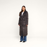 A woman stands against a plain white background wearing the Lizbeth Faux Fur Jacket in gray over a white top and blue jeans with black shoes.