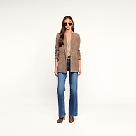 A woman stands facing forward against a plain white background, wearing sunglasses, the Aimee Oversized Suede Blazer in tan over a deep V-neck blouse, blue flared jeans, and leopard print shoes.