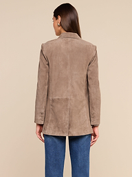 A woman stands with her back to the camera against a plain, light background, wearing the Aimee Oversized Suede Blazer in tan with blue jeans. Her straight brown hair falls to her shoulders.