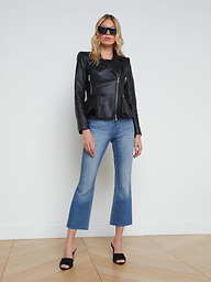 A woman wearing sunglasses, the Lyric Leather Peplum Jacket in black lambskin, blue cropped jeans, and black heels stands against a plain white background.