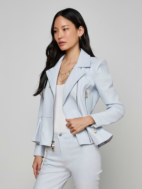 Wearing the Lyric Peplum Biker Jacket, a woman with long dark hair poses with one hand in her pocket against a plain, light background.