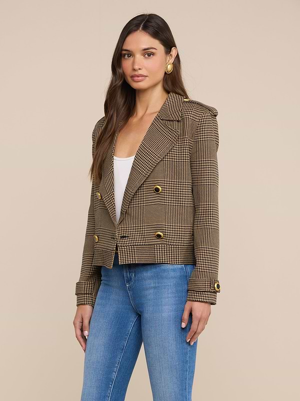 A woman with long brown hair wears the Xoey Cropped Trench Coat, styled over a white top and blue jeans. She stands facing forward against a plain light background.
