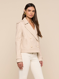 A woman stands facing forward, wearing the Xoey Cropped Leather Trench Coat in a cream hue with matching pants and gold earrings, set against a plain light background.