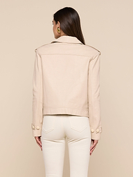 A woman with long brown hair, wearing gold earrings and off-white pants, is shown from the back against a plain white background modeling the Xoey Cropped Leather Trench Coat.