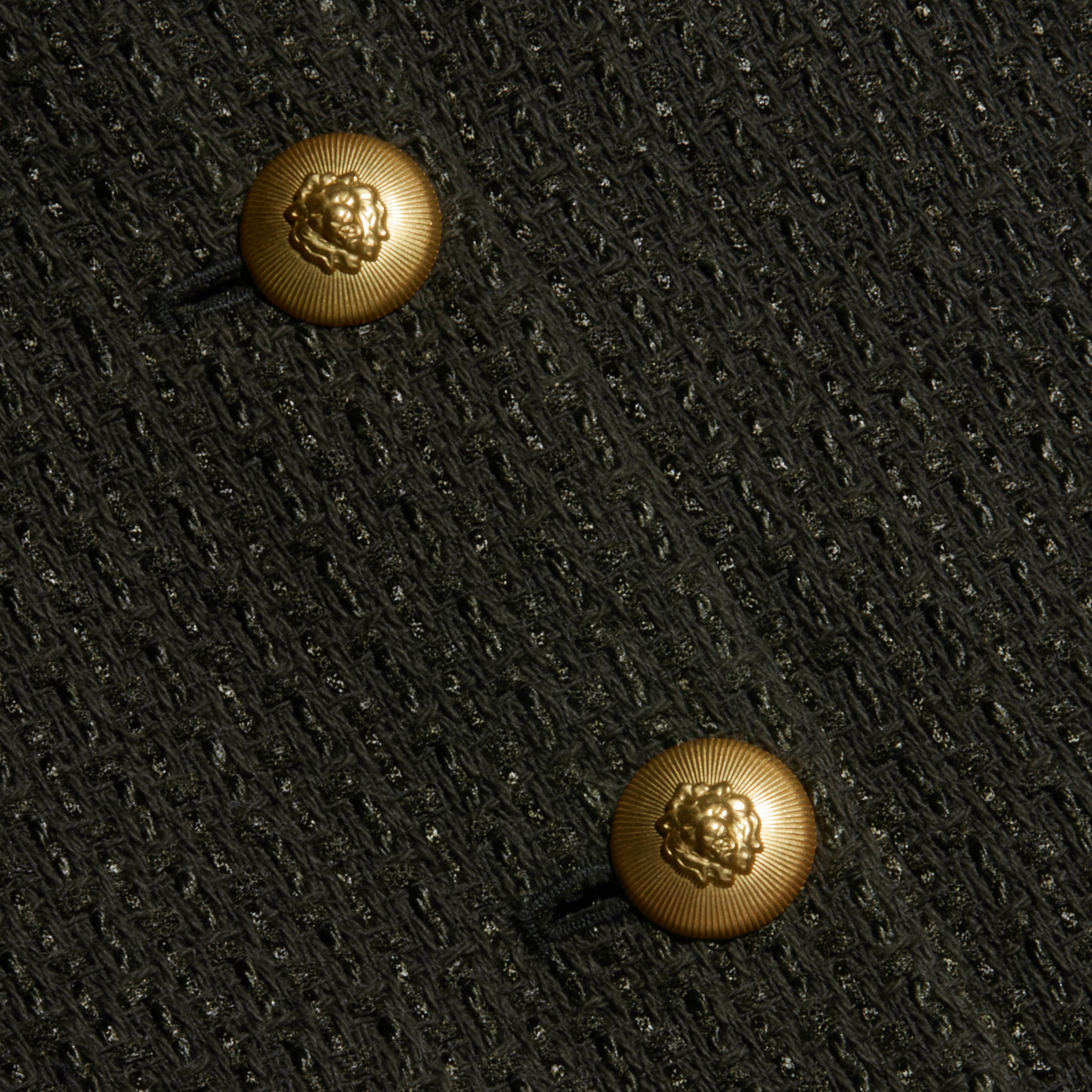 Close-up of two gold lion-embossed buttons on the textured black Zell Tweed Jacket.