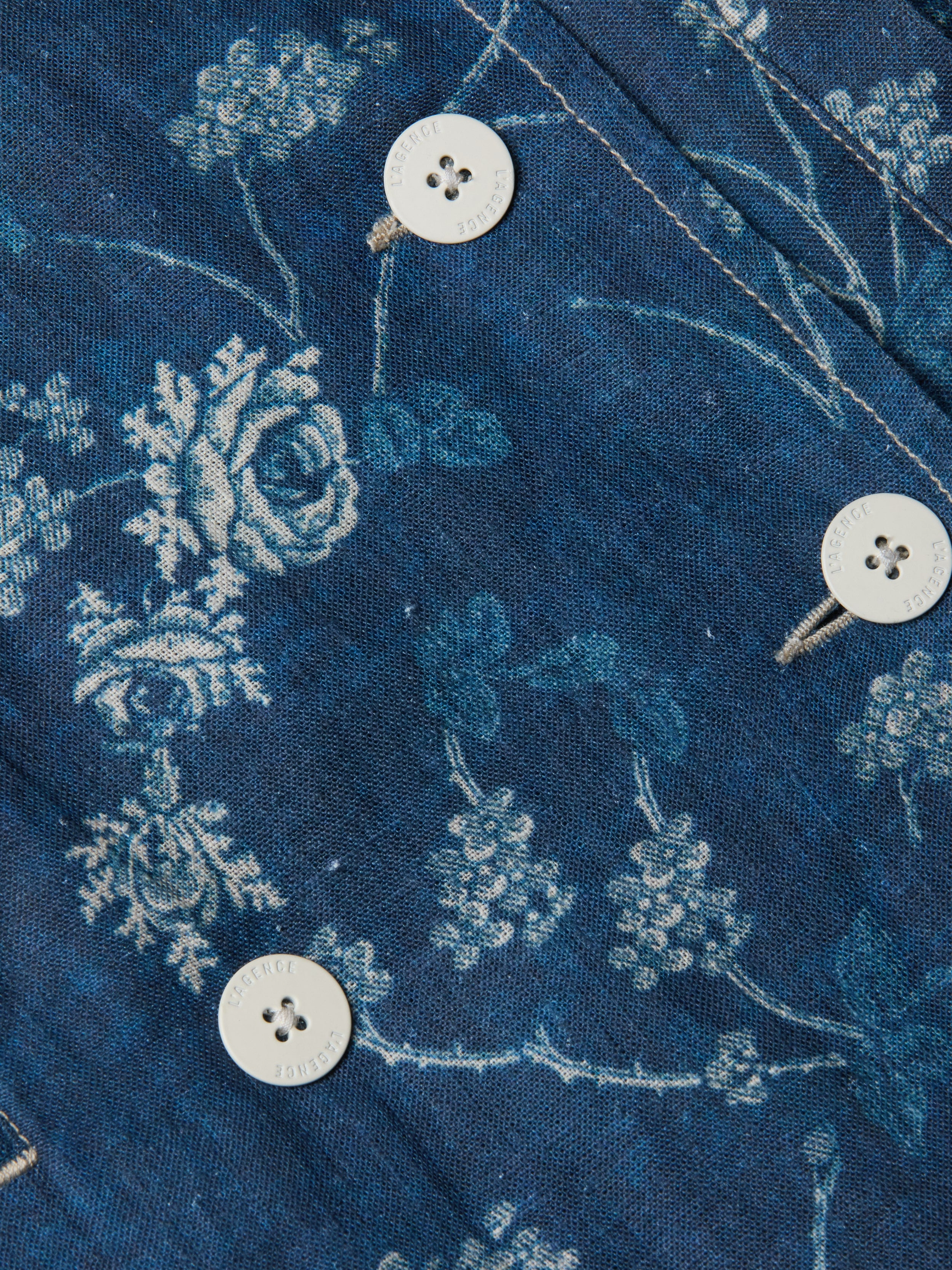 Close-up of the Bradley Linen Trench Coat in pure blue linen, featuring a white floral print, classic style, white buttons with visible stitching.