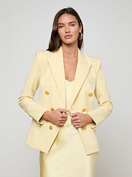 A woman stands facing forward against a plain white background, hands holding the front of her Kyomi Double-Breasted Blazer in yellow, styled over a matching dress.