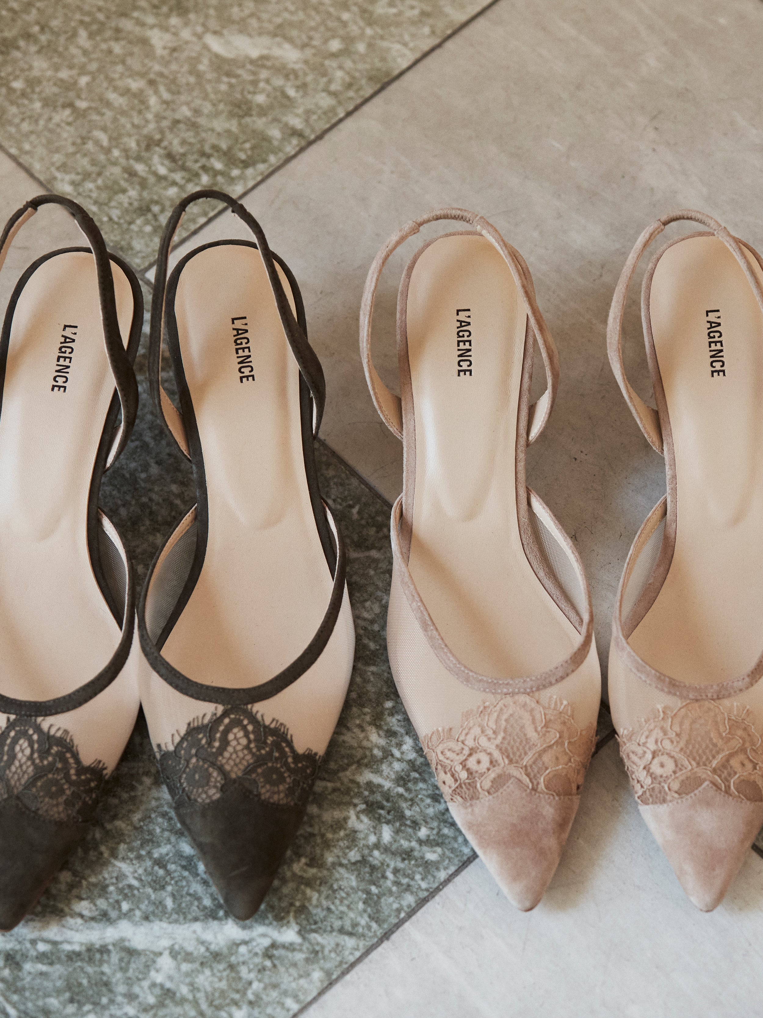 Two pairs of pointed-toe slingback heels with elegant lace detailing, one in black and beige, the other in blush pink and beige. Both pairs rest on a tiled floor and feature LAGENCE printed on the insole.