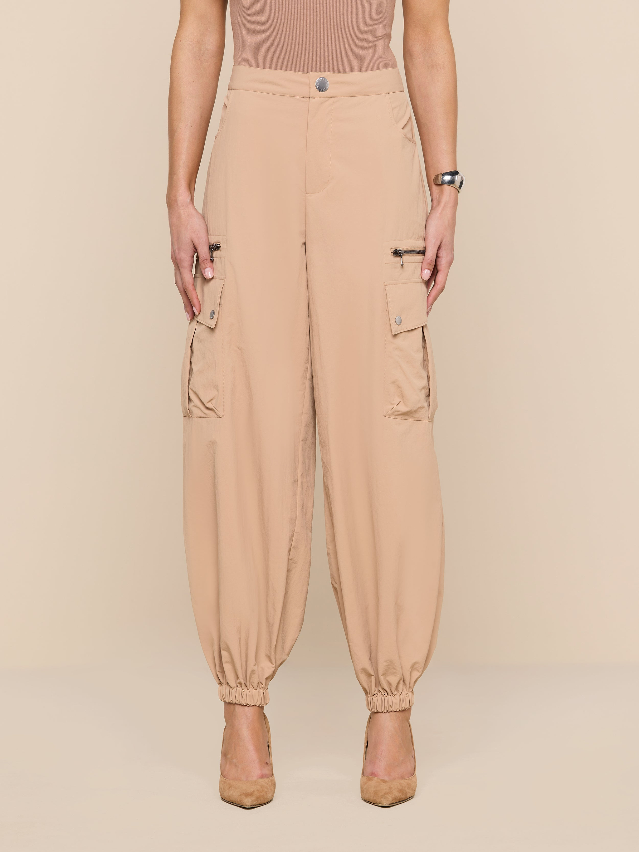 Wearing the Greer Nylon Jogger—beige cargo pants with elastic cuffs, modern jogger styling, water-repellent fabric, and cargo pockets—a person stands against a plain white background with their face not visible.