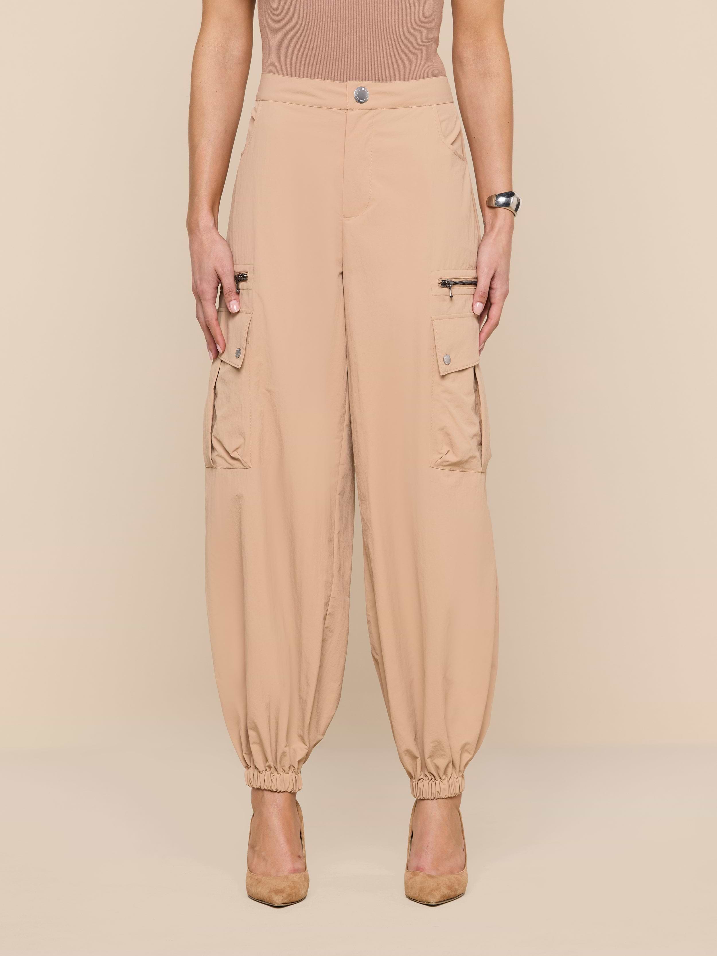 Wearing the Greer Nylon Jogger—beige cargo pants with elastic cuffs, modern jogger styling, water-repellent fabric, and cargo pockets—a person stands against a plain white background with their face not visible.