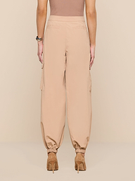 A person wearing the Greer Nylon Jogger—high-waisted, loose beige pants with cinched ankles—paired with tan heeled shoes, shown from the back against a plain white background.