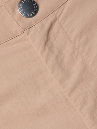 Close-up of the Greer Nylon Jogger, featuring light beige fabric with a visible seam and a metallic button engraved with text near the waistband, designed in a modern jogger style.
