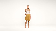 A woman stands against a plain white background, wearing a cream-colored sleeveless top, yellow knee-length skirt, and beige heels, with one hand in her skirt pocket.