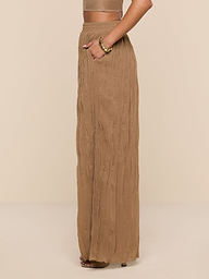 A person stands sideways with hands in pockets against a white background, wearing a tan crop top and the high-waisted, loose, sheer Ethel Pleated Pant.
