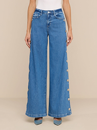 A person wears the Jennings Snap Wide-Leg Jean, featuring high-waisted, wide-leg styling in featherweight denim with large buttons along the outer seams, paired with pointed-toe blue shoes and a white top, standing against a plain white background.