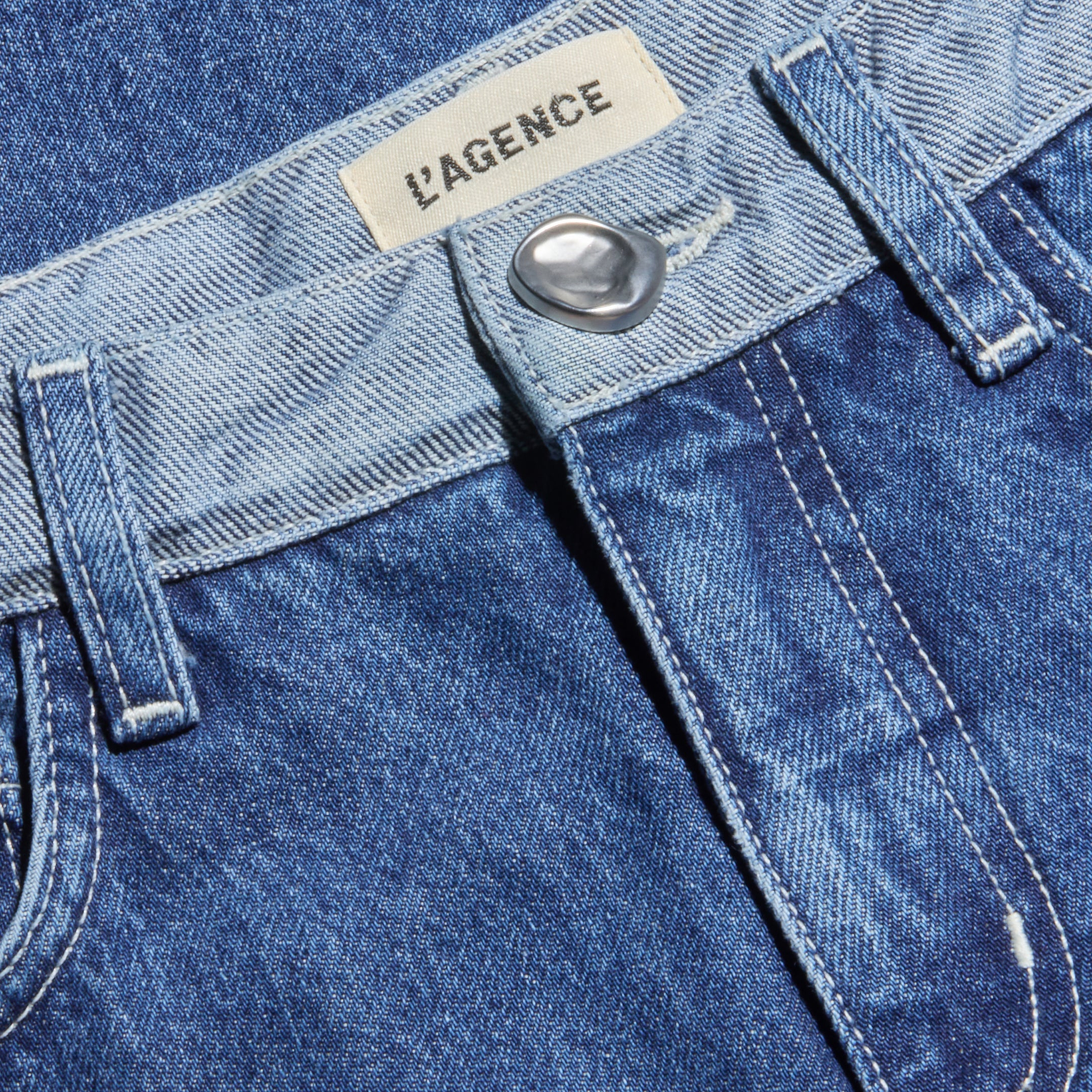 Close-up of the Bronte Cropped Wide-Leg Jean in blue denim, featuring a silver button, visible belt loops, and a label sewn inside the high waistband that reads L’AGENCE.