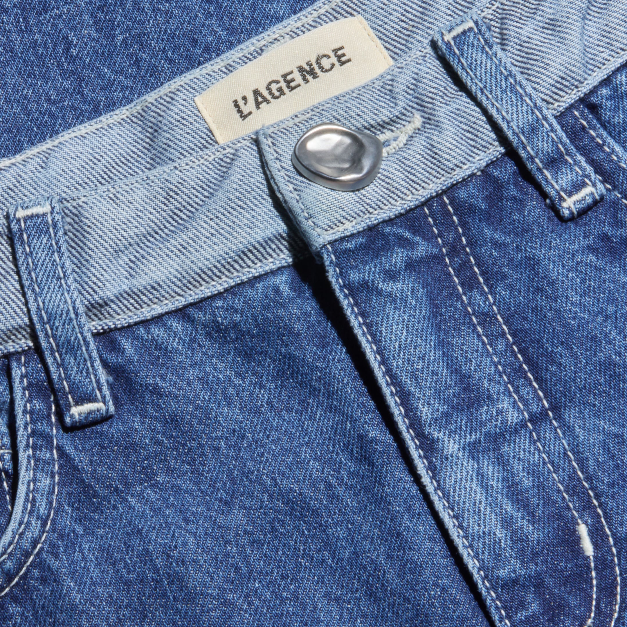 Close-up of the Bronte Cropped Wide-Leg Jean in blue denim, featuring a silver button, visible belt loops, and a label sewn inside the high waistband that reads L’AGENCE.