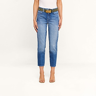 A person wearing a white top, the Avena Slim-Leg Jean in blue with a green belt featuring a brown buckle, and clear high-heeled shoes stands against a plain white background.