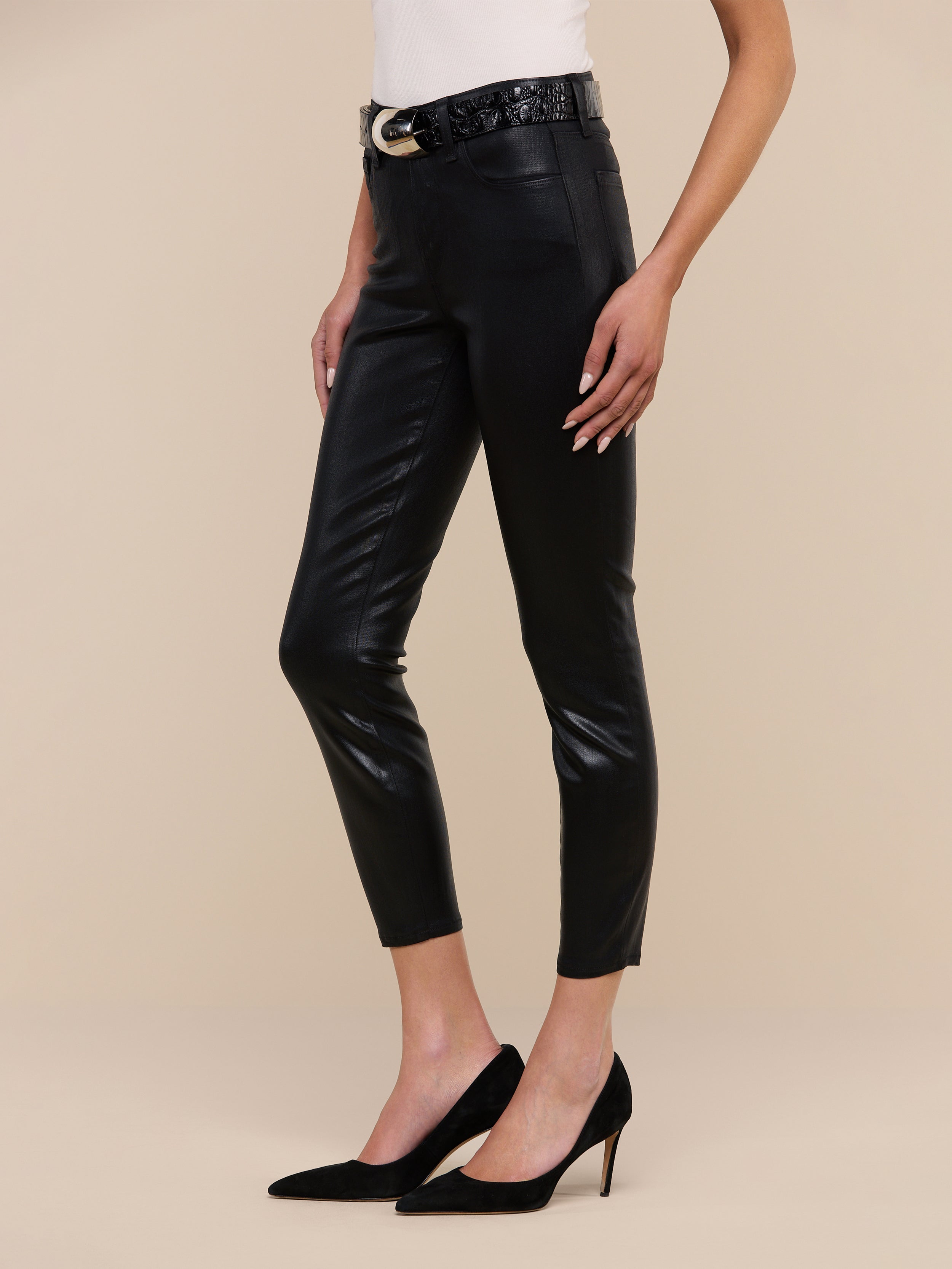 A person wearing the Margot Coated Cropped Skinny Jean, a light top, a black belt with a gold buckle, and black high-heeled shoes poses against a plain white background.
