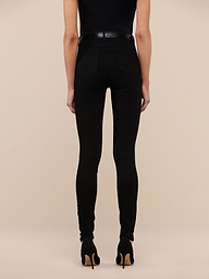 A person stands with their back to the camera against a plain white background, wearing the Marguerite Skinny Jean in black high-recovery fabric, styled with black high heels and a white top.