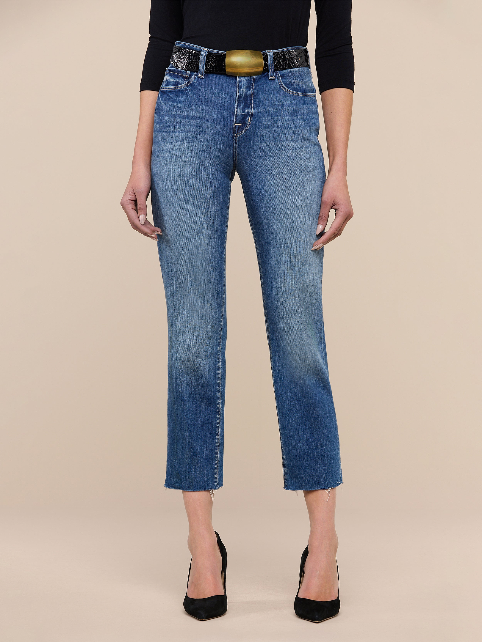 A person wearing the Sada Slim-Leg Cropped Jean, paired with black pointed heels, a black three-quarter sleeve top, and a wide belt stands against a plain white background.