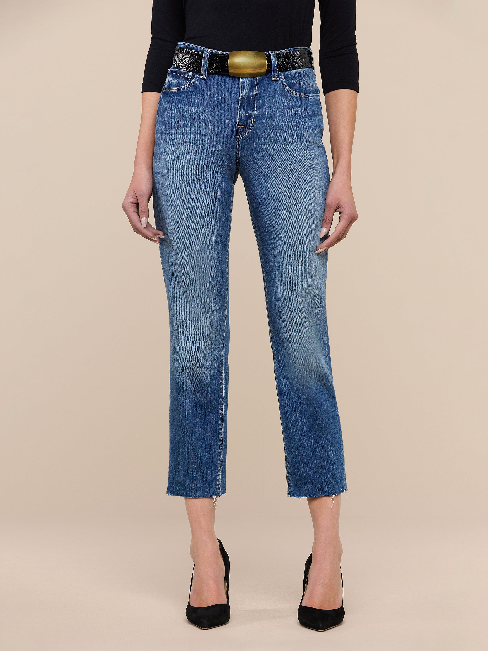A person wearing the Sada Slim-Leg Cropped Jean, paired with black pointed heels, a black three-quarter sleeve top, and a wide belt stands against a plain white background.