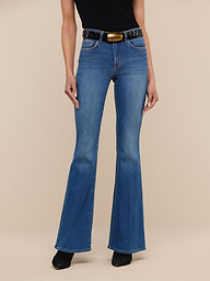 A person wearing the Bell Flare Jean in vintage-inspired blue premium stretch denim, styled with a black sleeveless top, a wide black belt featuring a large buckle, and black shoes, stands against a plain white background.