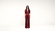A person wearing sunglasses and a burgundy jumpsuit stands against a plain white background, hands by their sides, facing forward.
