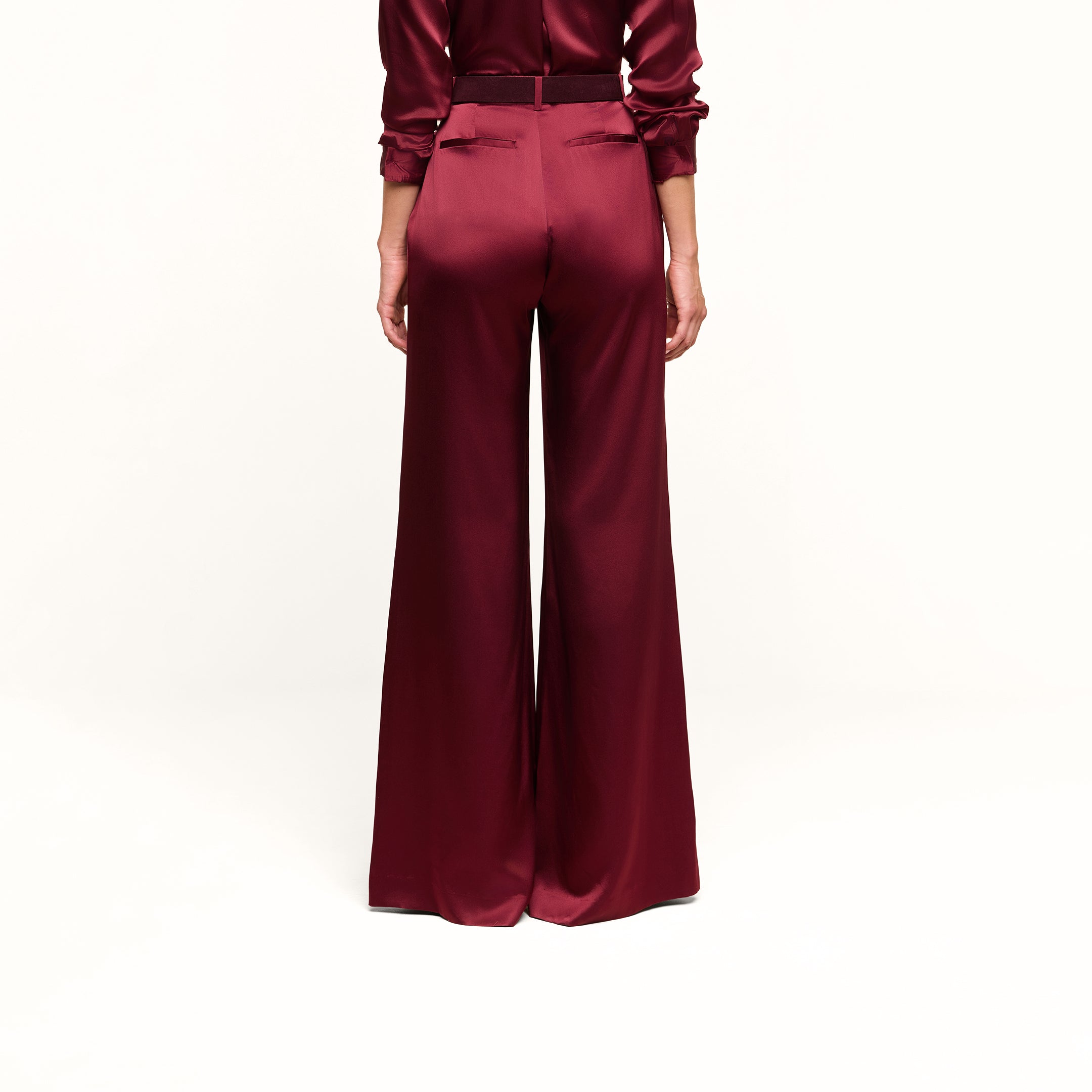 A person shown from the back stands against a plain white background, wearing the high-rise Pilar Silk Wide-Leg Pant in burgundy satin paired with a matching blouse.
