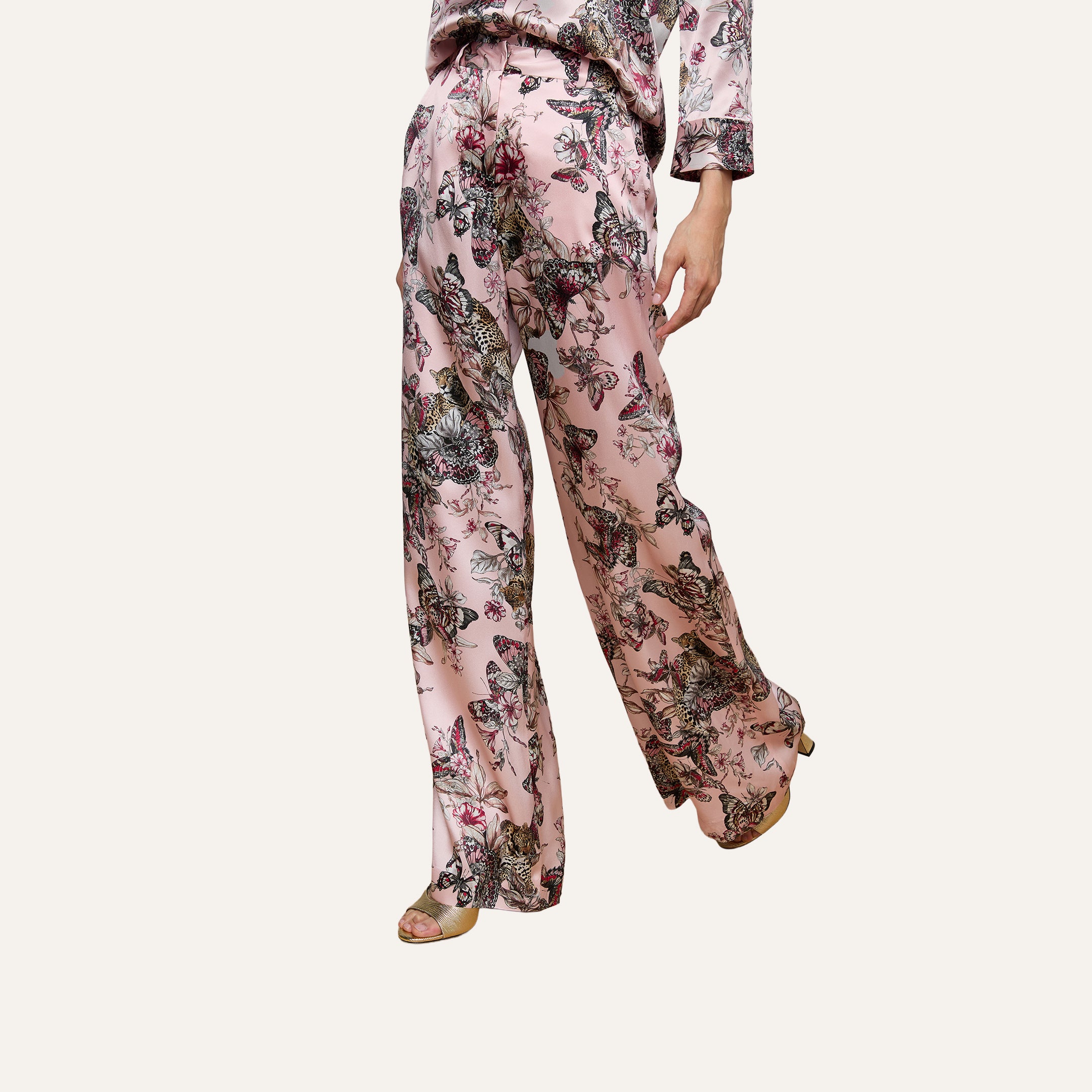 Person wearing the Pilar Silk Wide-Leg Pant, featuring a pink floral pattern and a high-rise, loose silhouette. Only the lower body and one hand are visible against a plain light background.