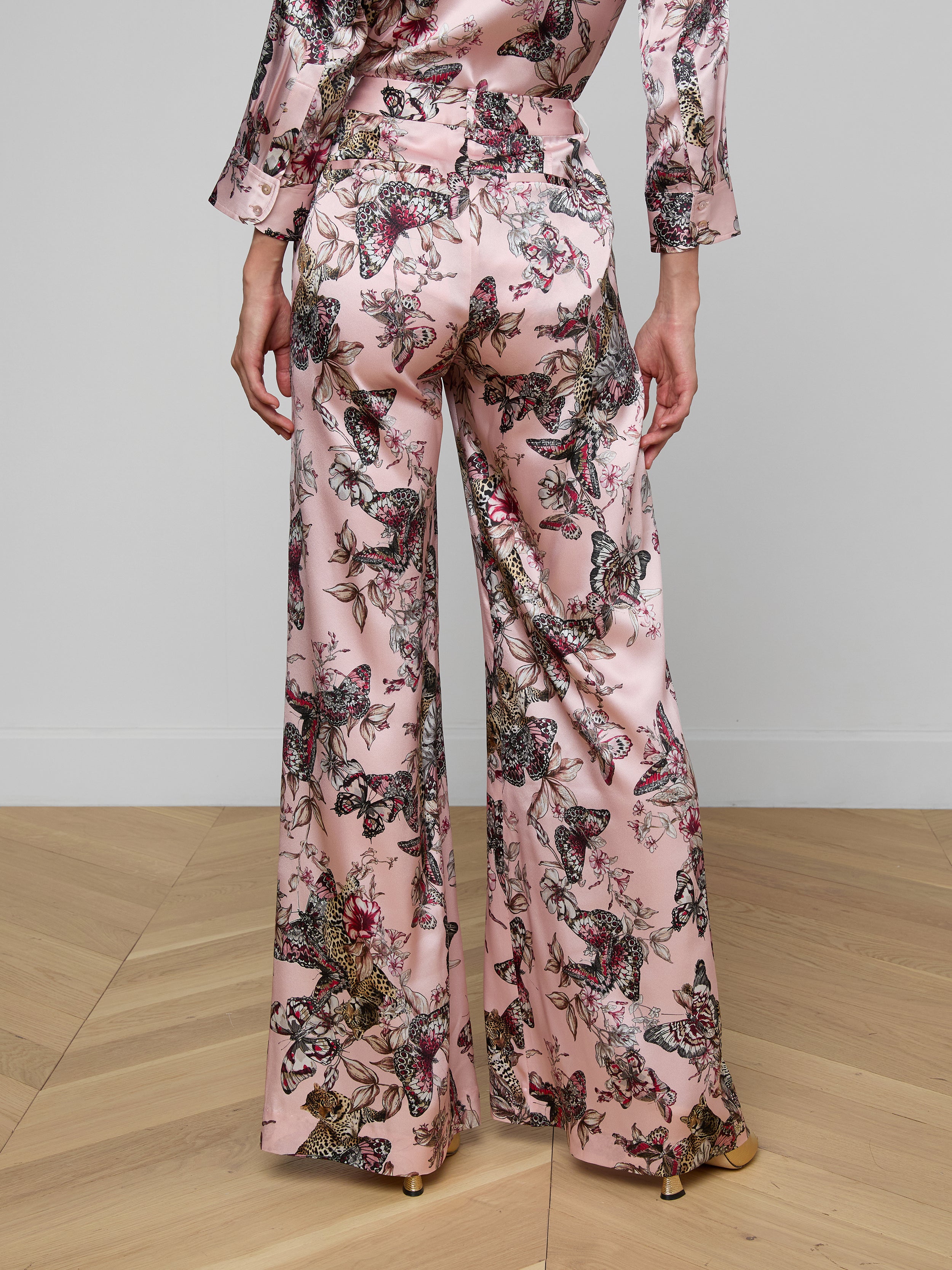 A person wearing the Pilar Silk Wide-Leg Pant in a pink, butterfly jungle print satin, shown from the back against a plain background.