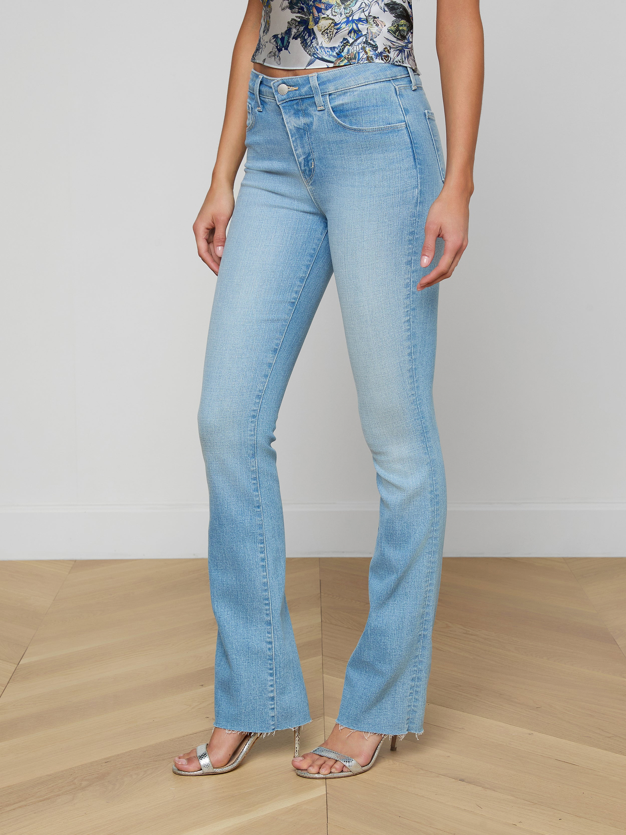 Wearing the Ruth Straight-Leg Jean in a light blue, vintage wash with slight fading, styled with a floral top and silver open-toe heels, a person stands against a plain white background.
