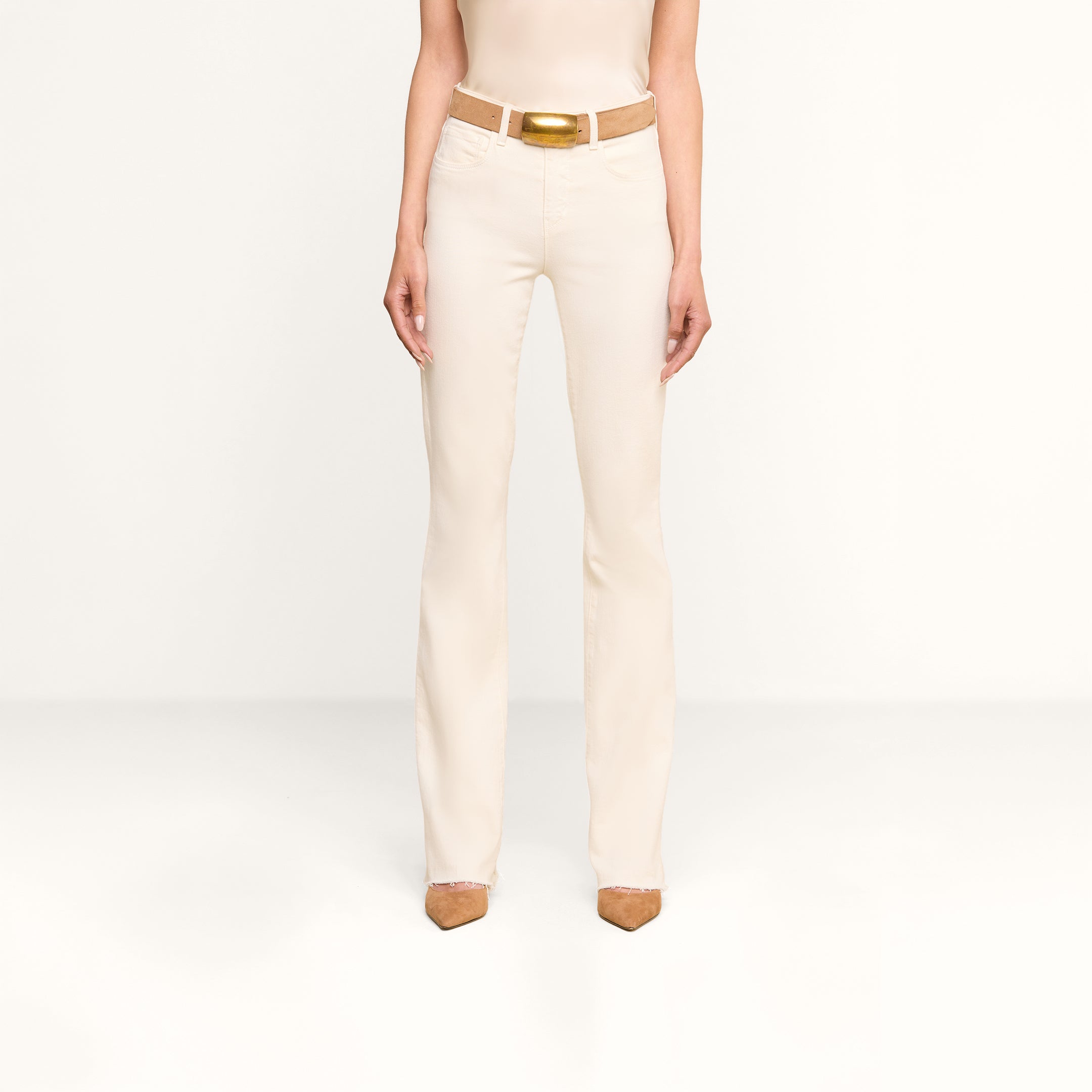 Su uno sfondo beige, una persona indossa i jeans Ruth Straight-Leg in denim elasticizzato bianco vintage, abbinati a una cintura coordinata con fibbia dorata, un top senza maniche e scarpe color cuoio a punta. Limmagine la ritrae dalle spalle ai piedi.
