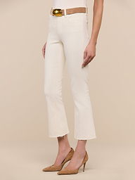 Wearing the Kendra Cropped Flare Jean in vintage white, styled with a tan belt and tan high-heeled shoes, a person stands against a plain white background.