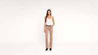 Woman stands against a plain white background, wearing a white tank top, beige corduroy pants, black belt, and black shoes, with one hand in her pocket.