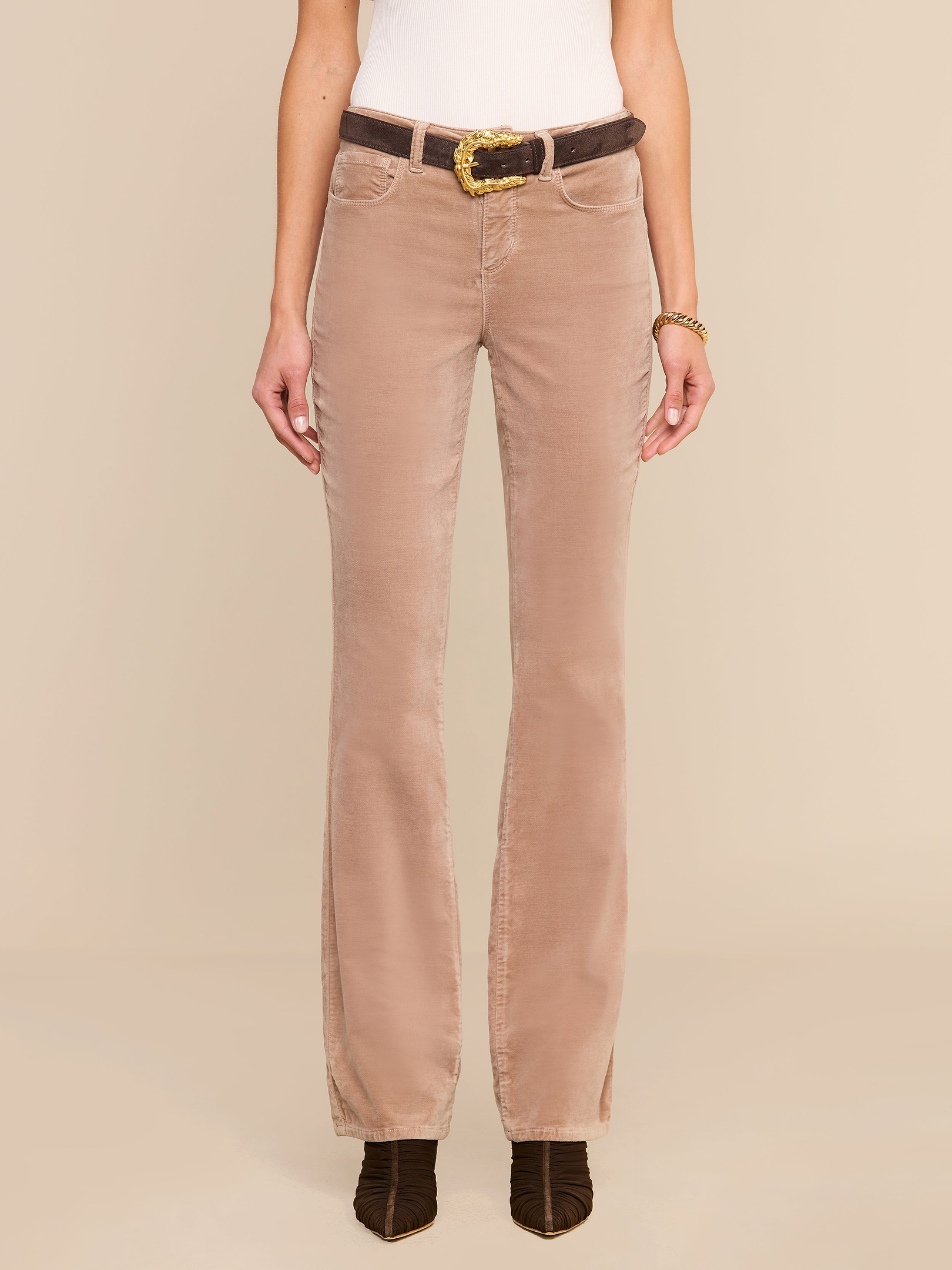 A person wearing the Stevie Velvet Jean styled in a high rise fit, paired with a white top, a brown belt, and dark brown shoes, stands against a plain white background. The image highlights the outfit from shoulders to feet.