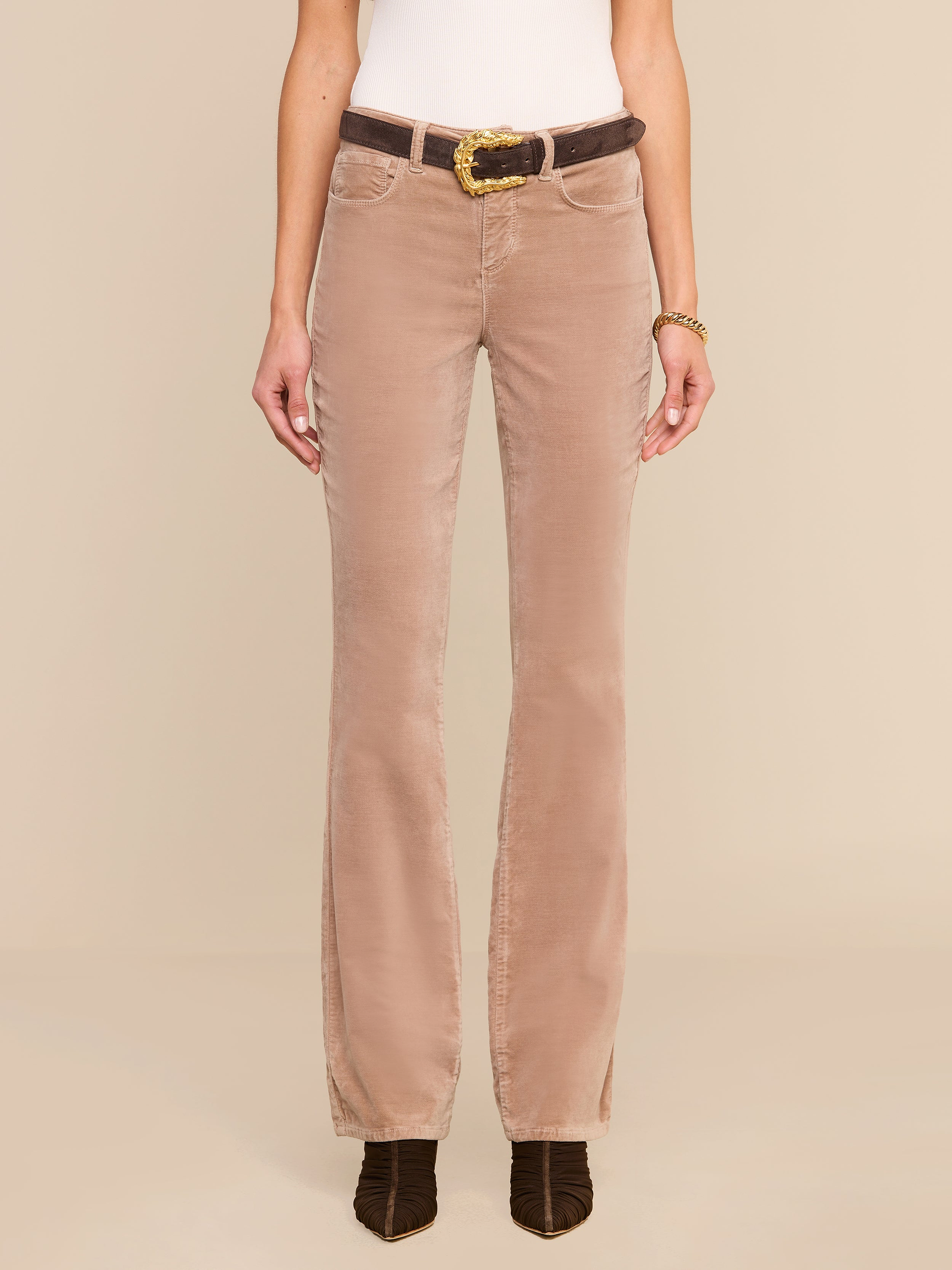 A person wearing the Stevie Velvet Jean styled in a high rise fit, paired with a white top, a brown belt, and dark brown shoes, stands against a plain white background. The image highlights the outfit from shoulders to feet.