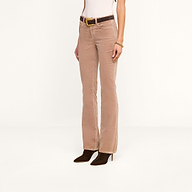 A person wearing the Stevie Velvet Jean in light brown, styled with a white top, a dark brown belt featuring a gold buckle, a bracelet, and dark heeled boots stands against a plain white background.