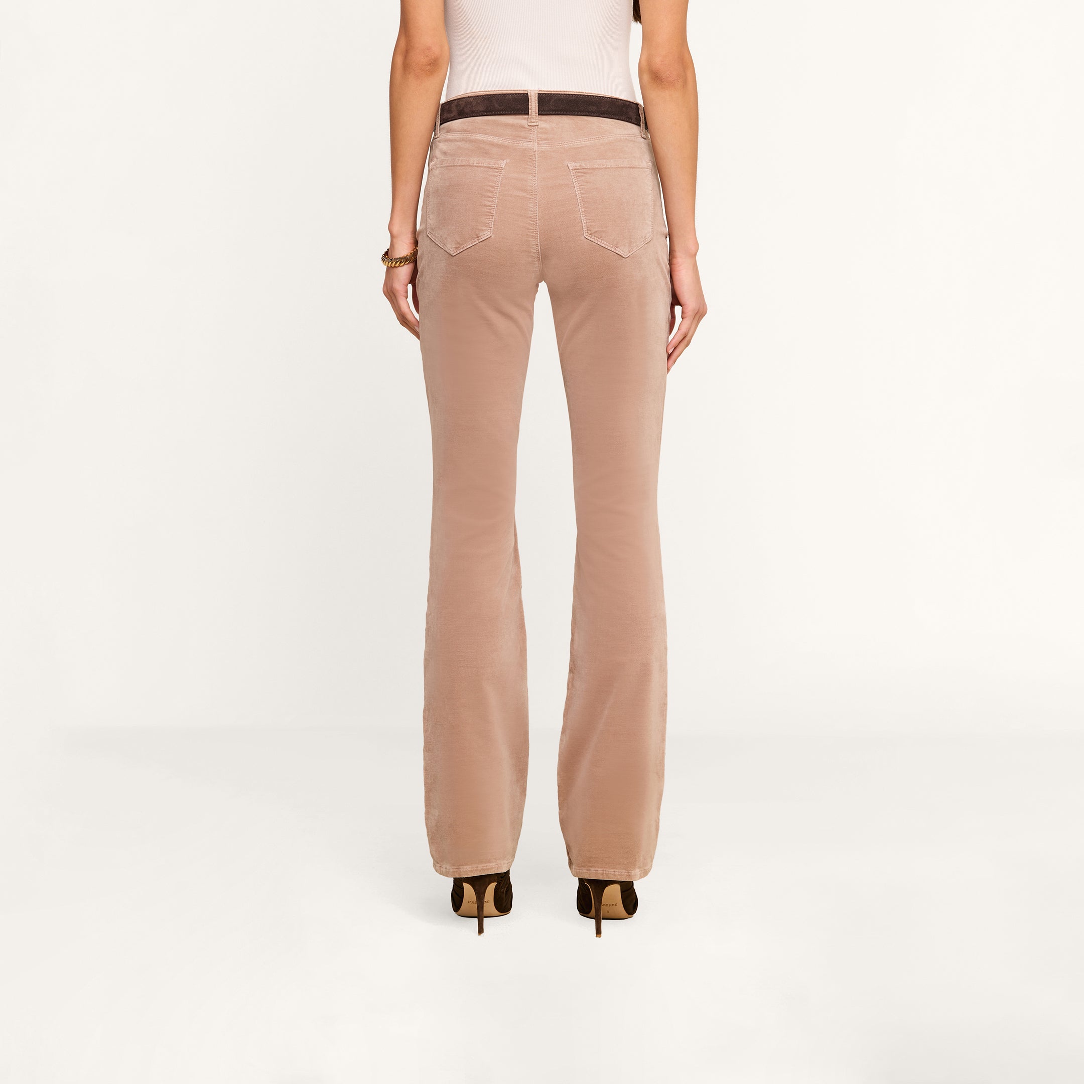 A person is shown from the back, wearing high-heeled shoes and the Stevie Velvet Jean in light brown, standing against a plain white background.