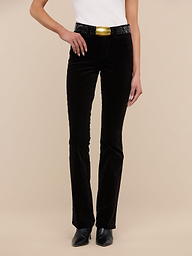A person wearing a white sleeveless top, the Stevie Velvet Jean in black, black shoes, and a large gold belt buckle stands against a plain white background.