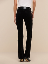 A person wearing black Stevie Velvet Jeans, a white sleeveless top, and black heeled shoes stands facing away against a plain white background.
