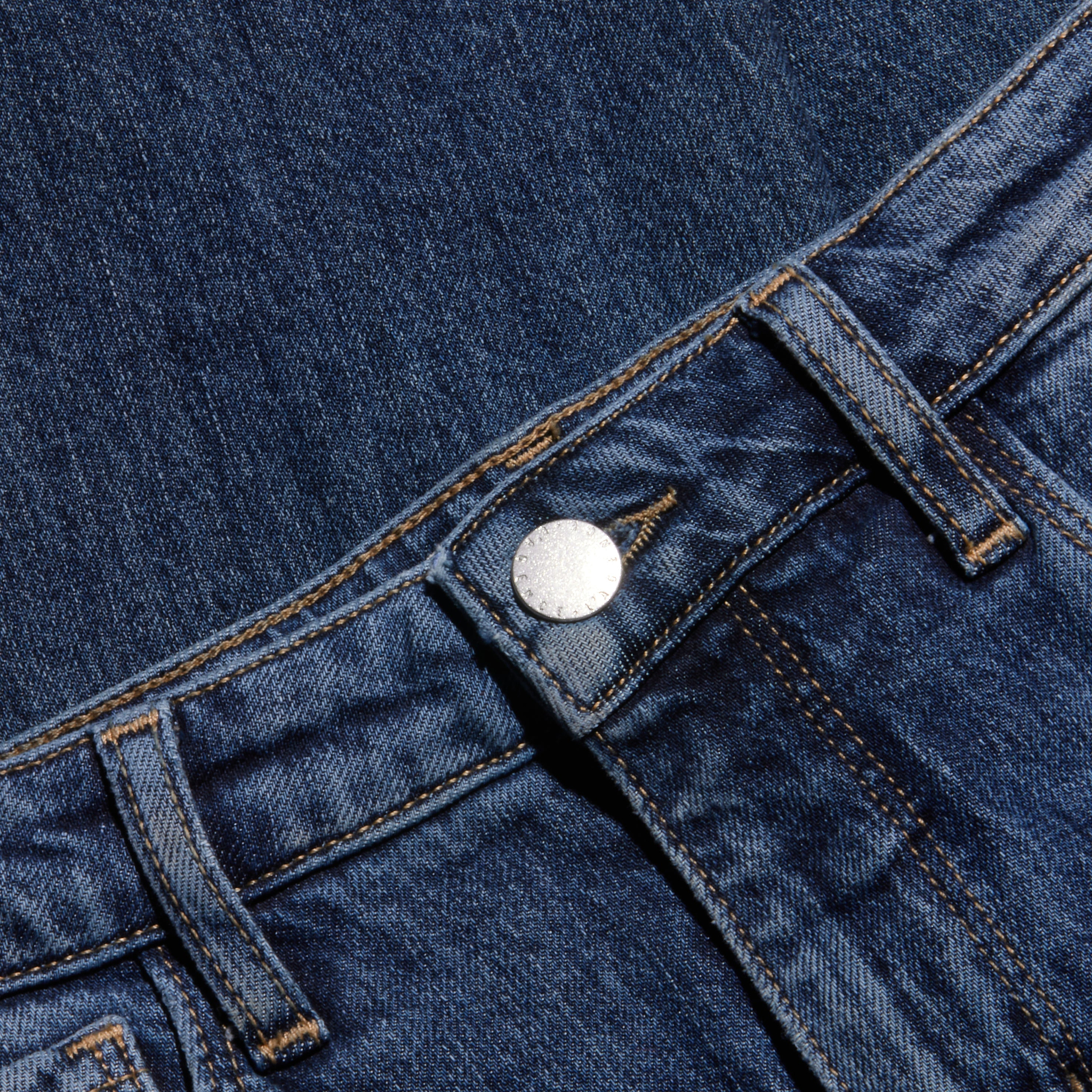 A close-up of blue denim jeans highlights the waistband, metal button, belt loops, and visible stitching against a coordinating denim background.