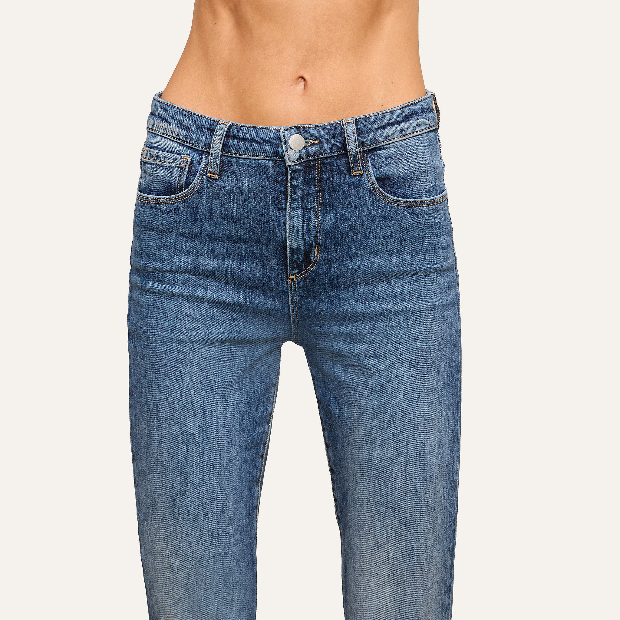 A close-up of a person in high-waisted blue jeans highlights their waist and lower torso against a plain light background.