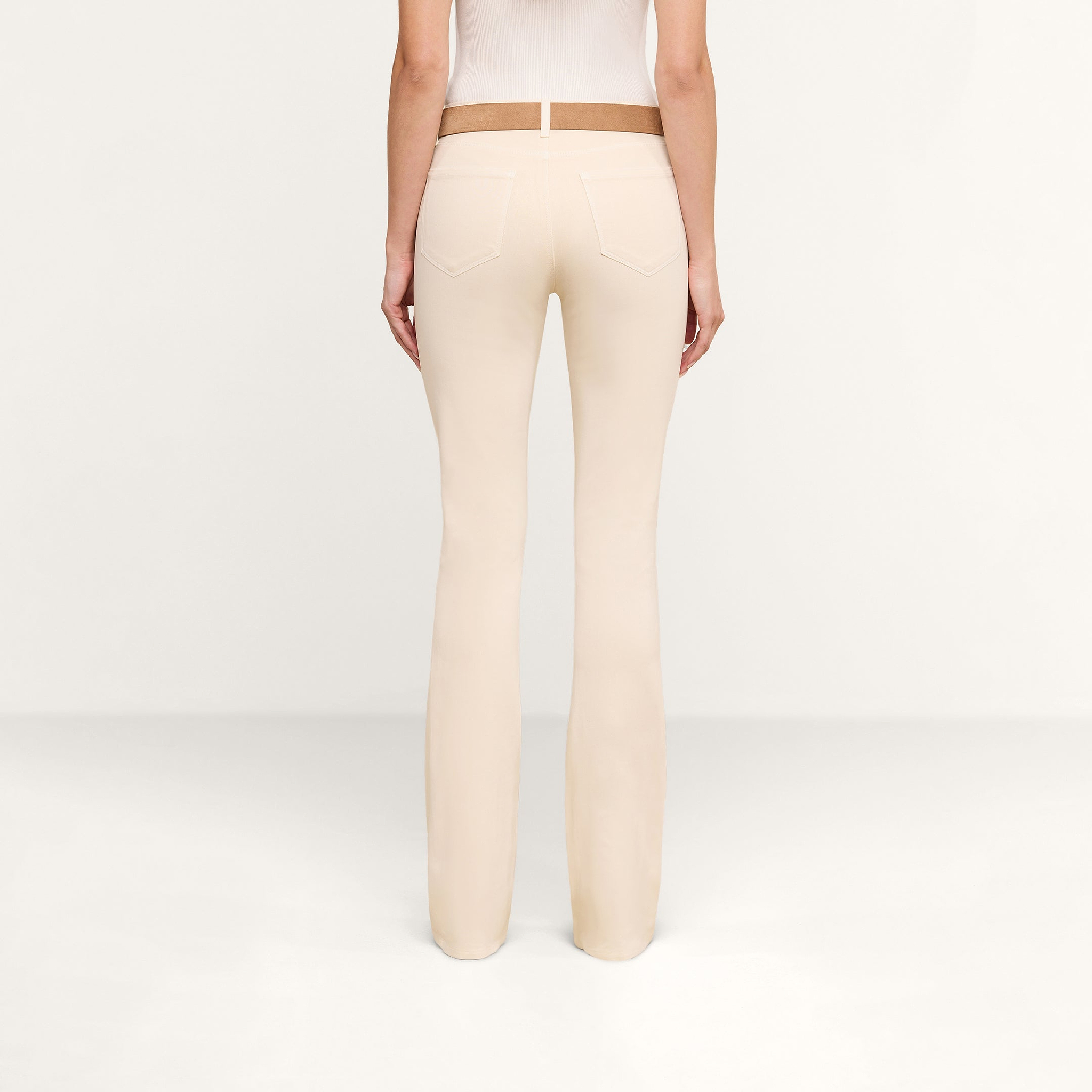 A person is shown from the back, standing in a plain, light-colored room, wearing the Selma Coated Bootcut Jean and a white top.