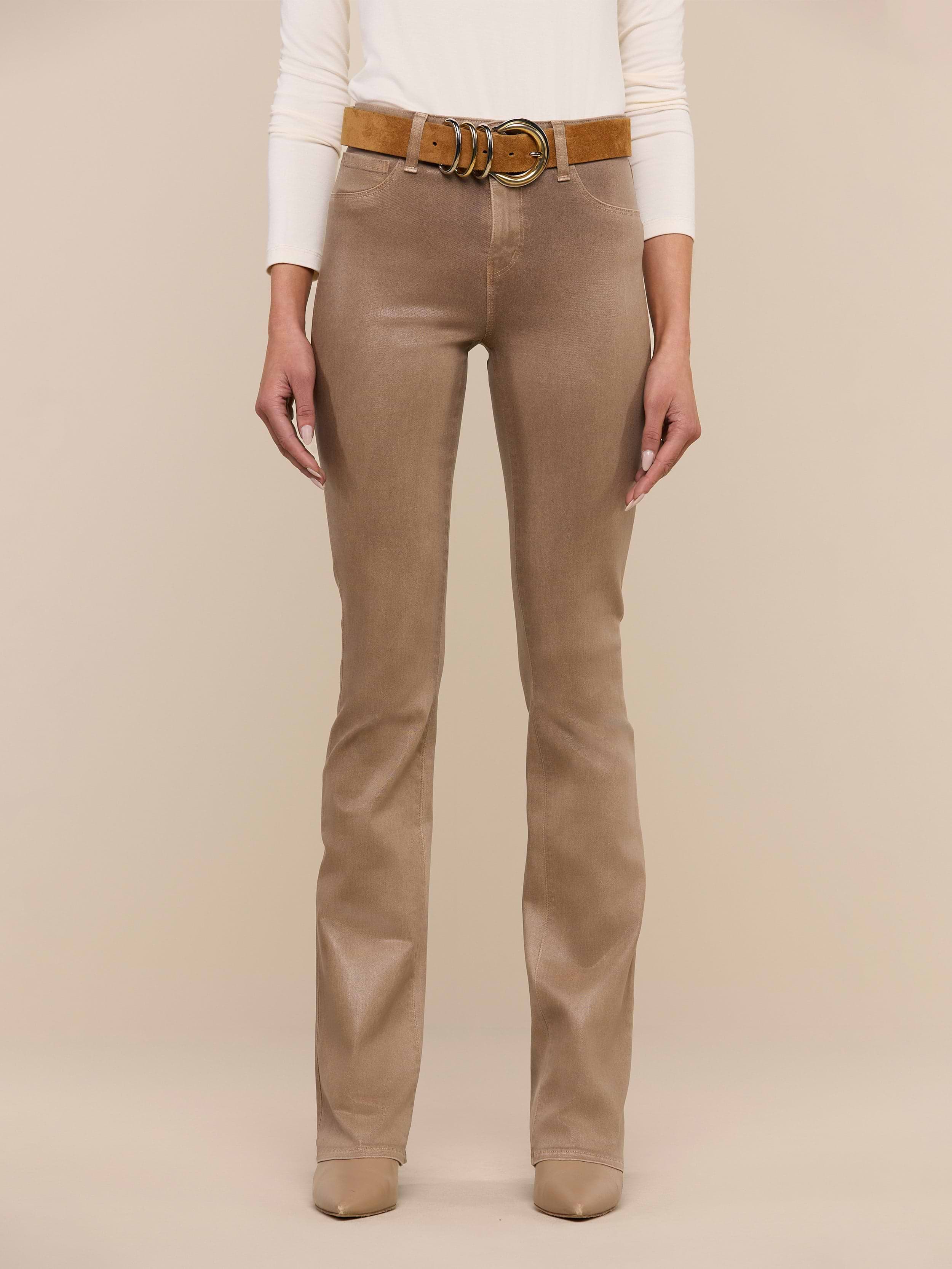 A person wearing the Selma Coated Bootcut Jean, styled with a brown belt and beige shoes, stands against a plain white background. Only the lower half of the body is visible.