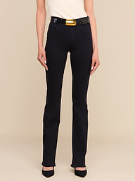 A person wearing the Selma Bootcut Jean in true black, paired with a light top, black heels, and a black belt featuring a large gold buckle stands against a plain white background. Only the lower half of the body is visible.
