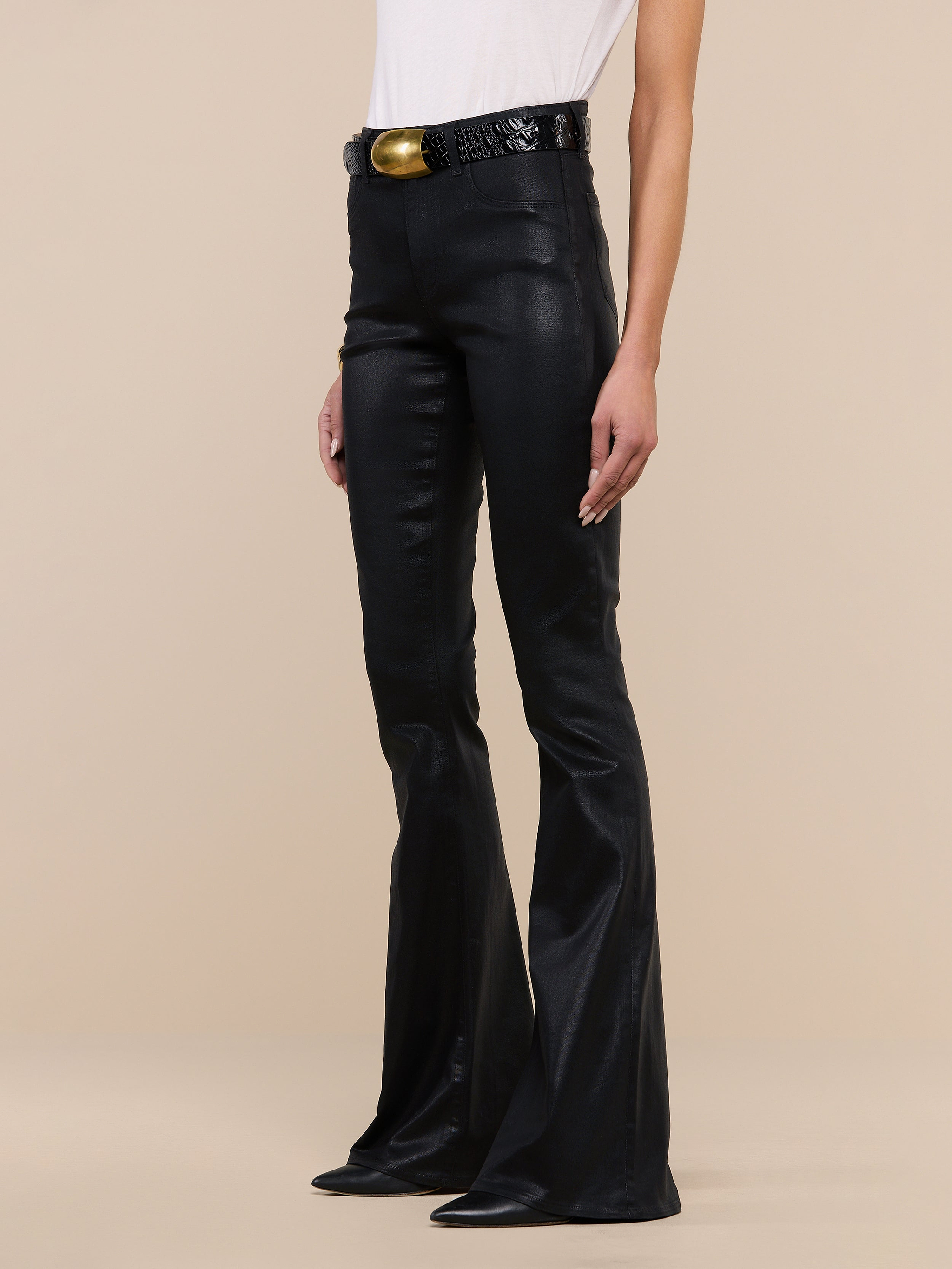 Person wearing the Marty Coated Flare Jean, styled with a black textured belt featuring a large gold buckle and a white top, standing against a plain white background. Only the lower half of their body is visible.