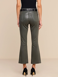 A person stands facing away against a plain white background, wearing the Kendra Coated Cropped Flare Jean in ash olive green, paired with a black belt, a black top, and black high-heeled shoes.