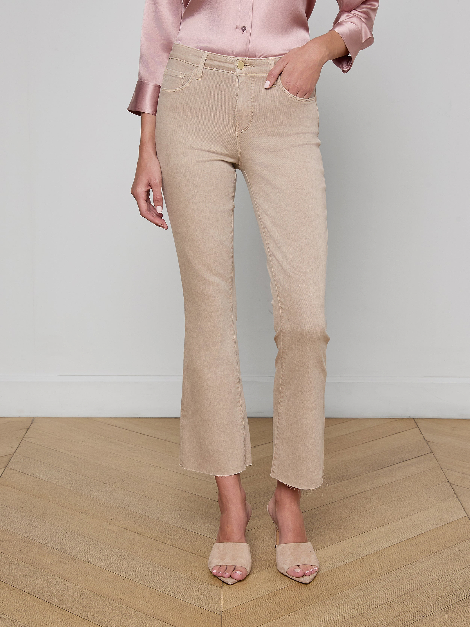 A person wearing the Kendra Cropped Flare Jean in neutral tan, paired with a light pink satin blouse and beige heeled sandals, stands against a plain light background.